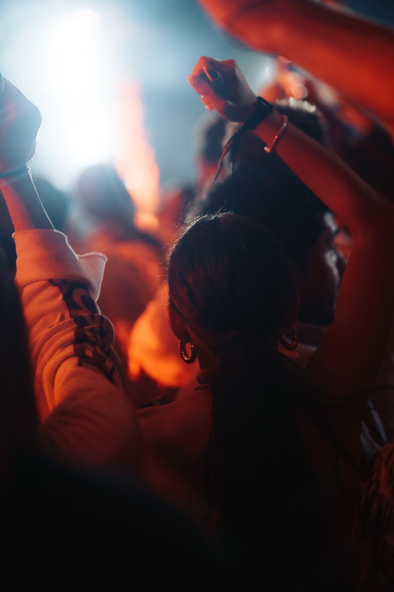 Close detail of a festival crowd, hands raised, warm stage light in the background