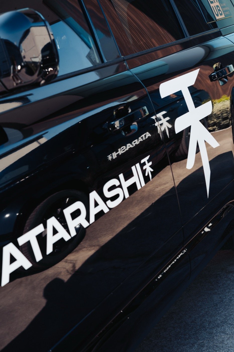 Close-up of the ATARASHI branding and logo on the side of a black Land Rover Defender