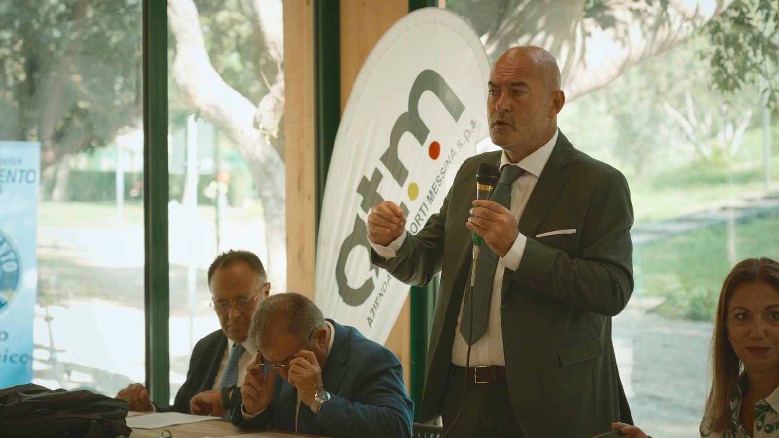 Un relatore parla accanto a una bandiera brandizzata ATM Messina durante una presentazione istituzionale
