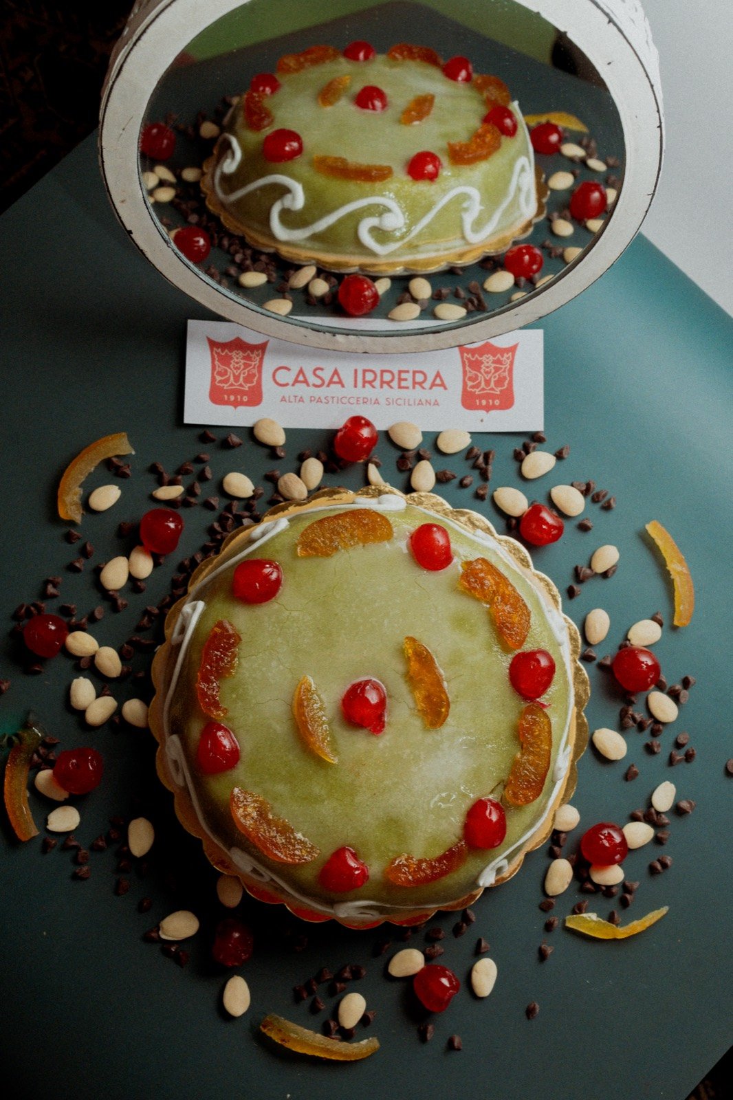 Casa Irrera pastry with pale green icing and candied fruit, reflected in a mirror above the branded table card