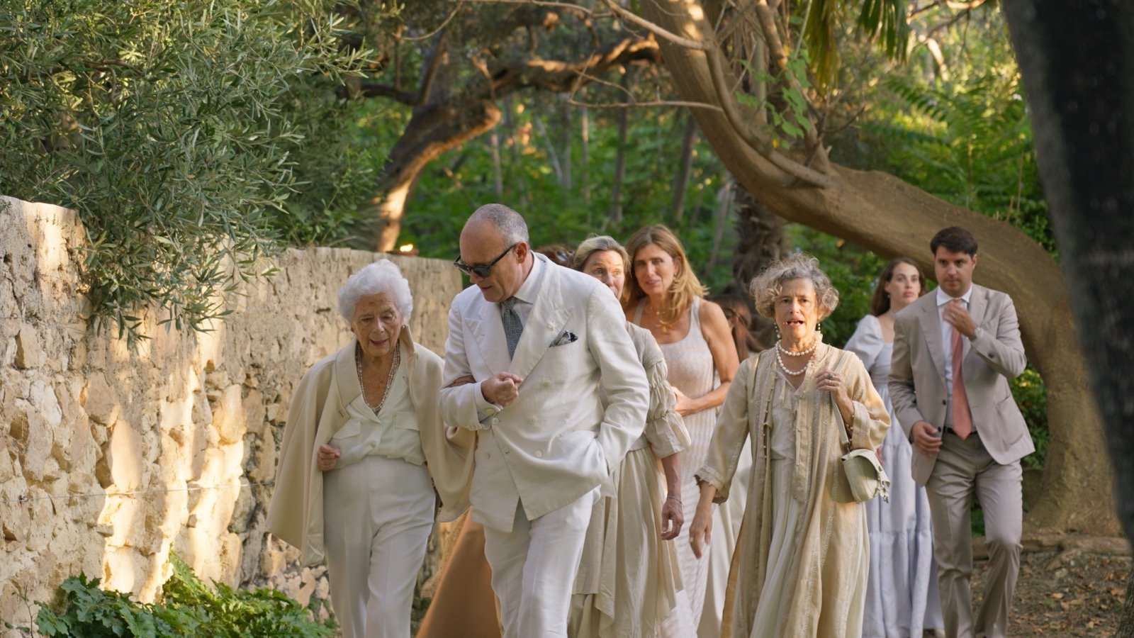 Elderly guests being walked in arm-in-arm along a garden path before the ceremony