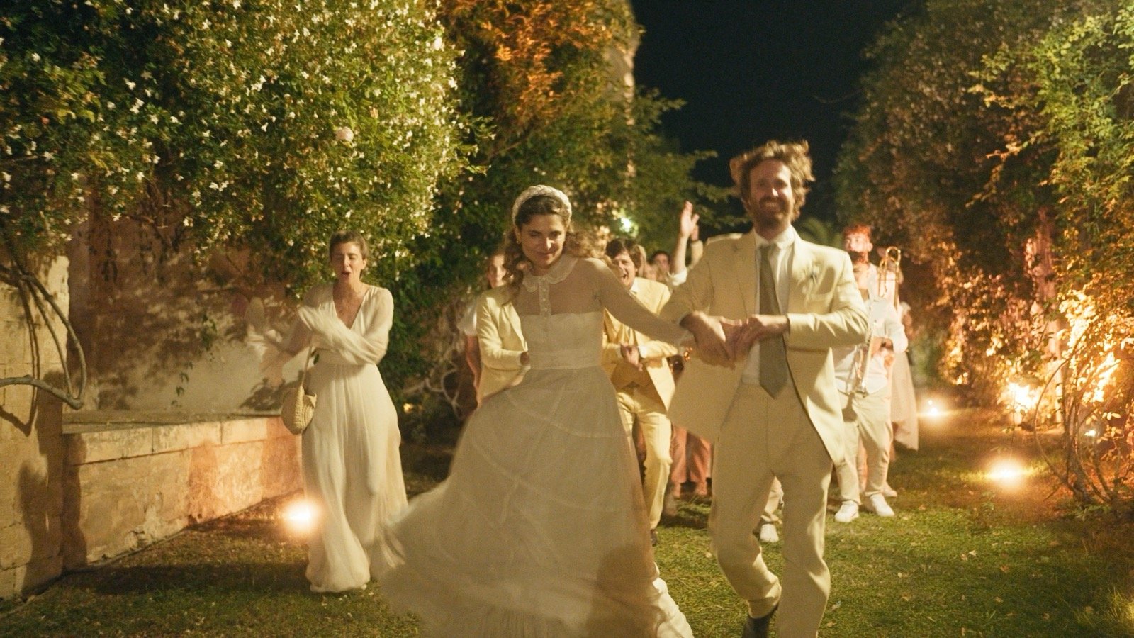 The bride and groom dancing together at night, surrounded by guests and string lights