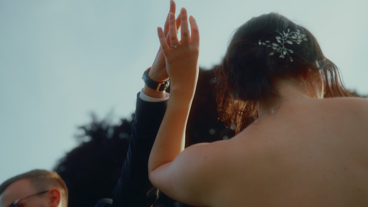 The bride from behind, arm raised, dancing at golden hour