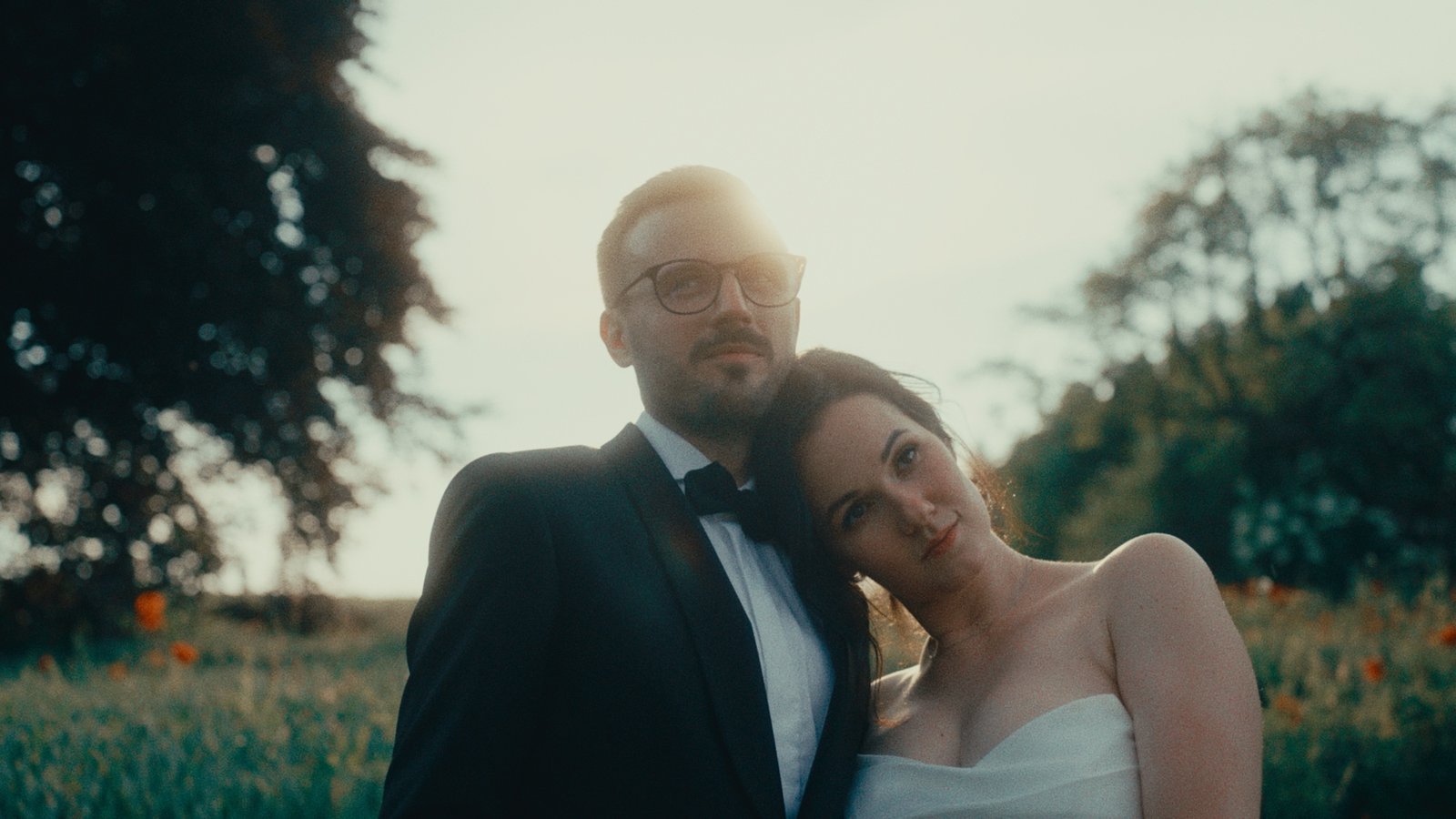 Ritratto degli sposi in un campo di papaveri all'ora dorata, la sposa appoggiata alla spalla dello sposo