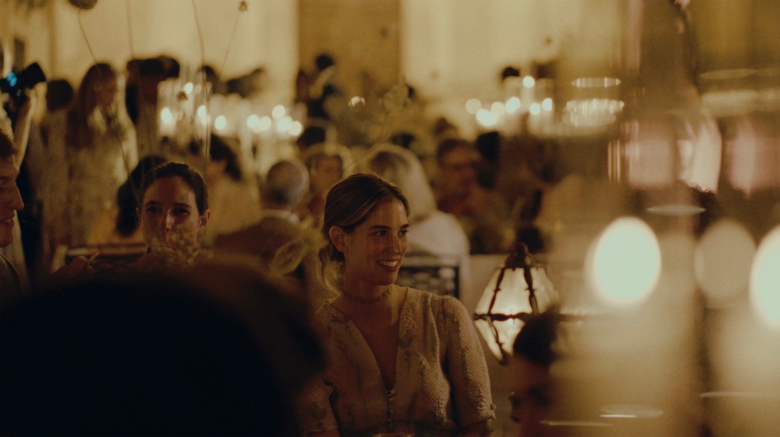 Guests at a candlelit dinner reception, smiling and talking under lantern light