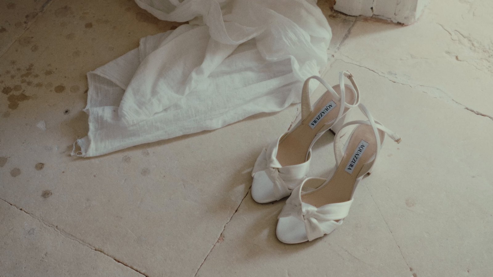 The bride's gown and white heels laid out on a stone floor before the ceremony