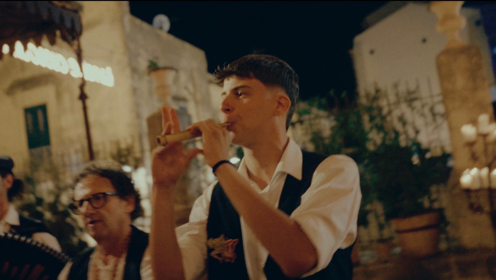 A musician playing a wind instrument in the street at night, part of the live band