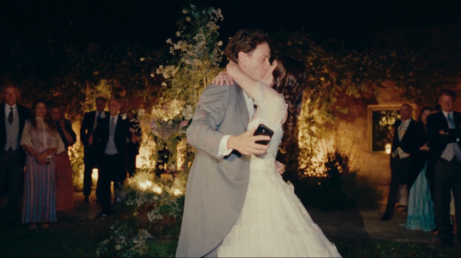 The newlyweds kissing at night as guests applaud in a candlelit garden