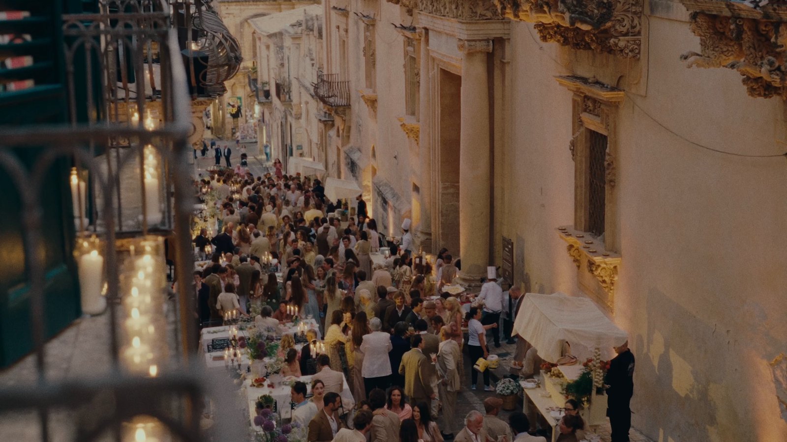 A long candlelit banquet table running the length of a narrow baroque street at night