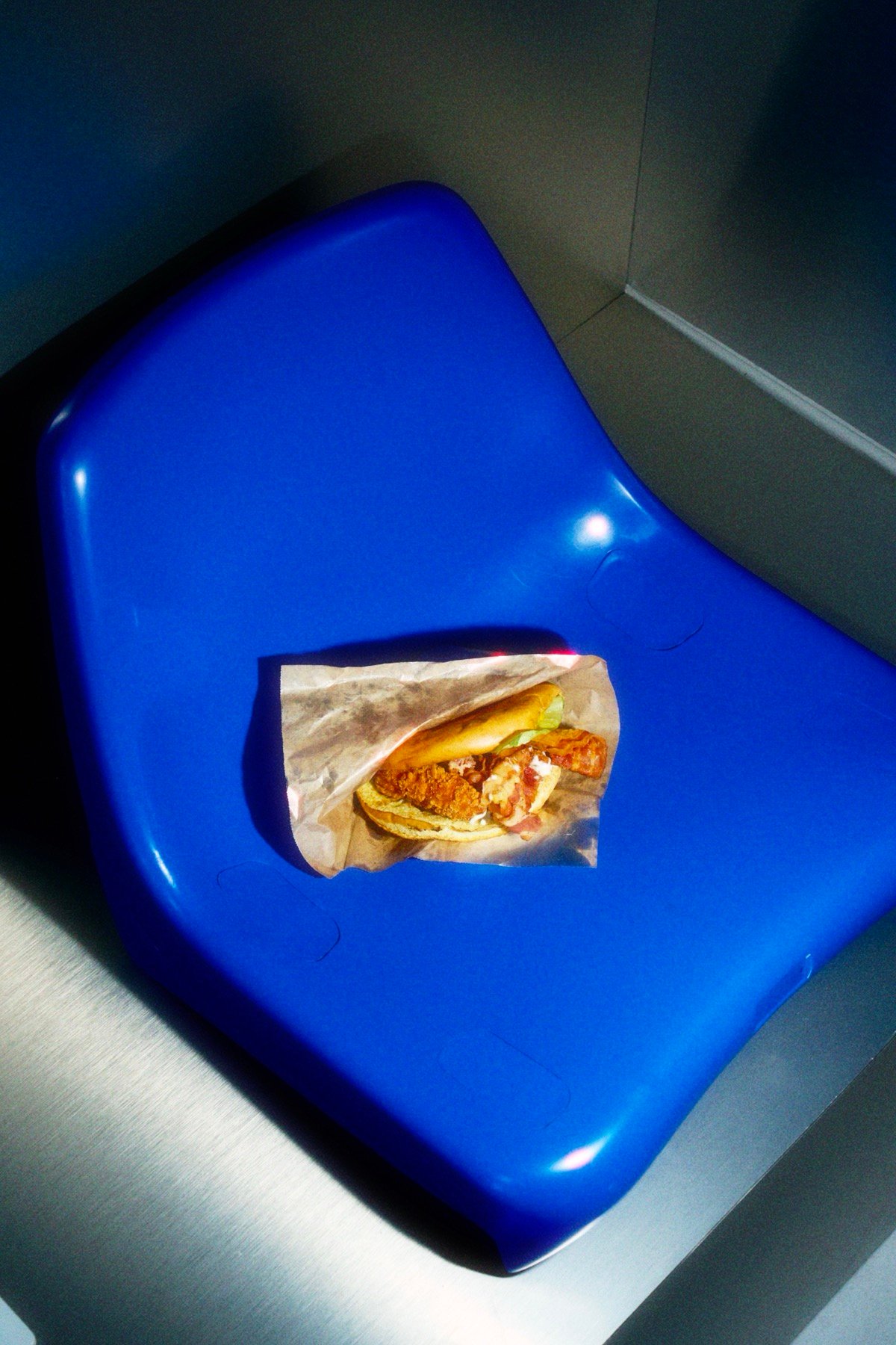 A wrapped fried chicken sandwich resting on a blue stadium seat