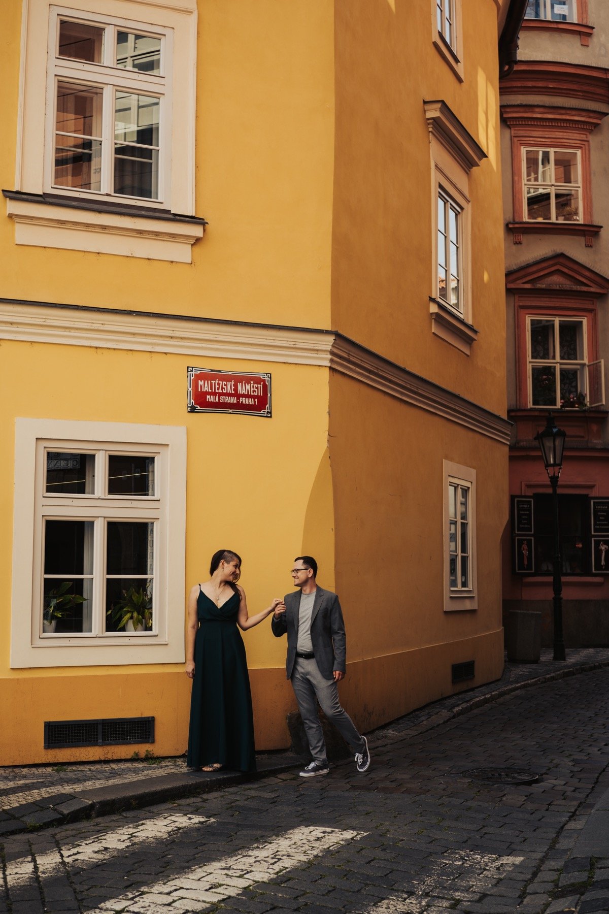 Couple holding hands on a cobbled street corner at Maltézské náměstí, Prague