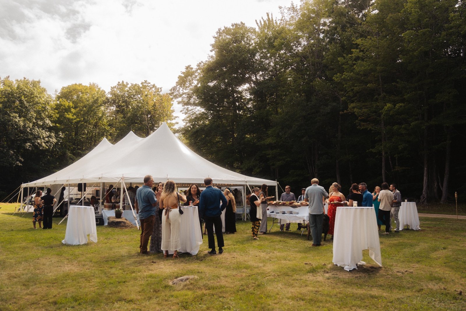 Wedding guests gathered under a white tent at a New England forest reception