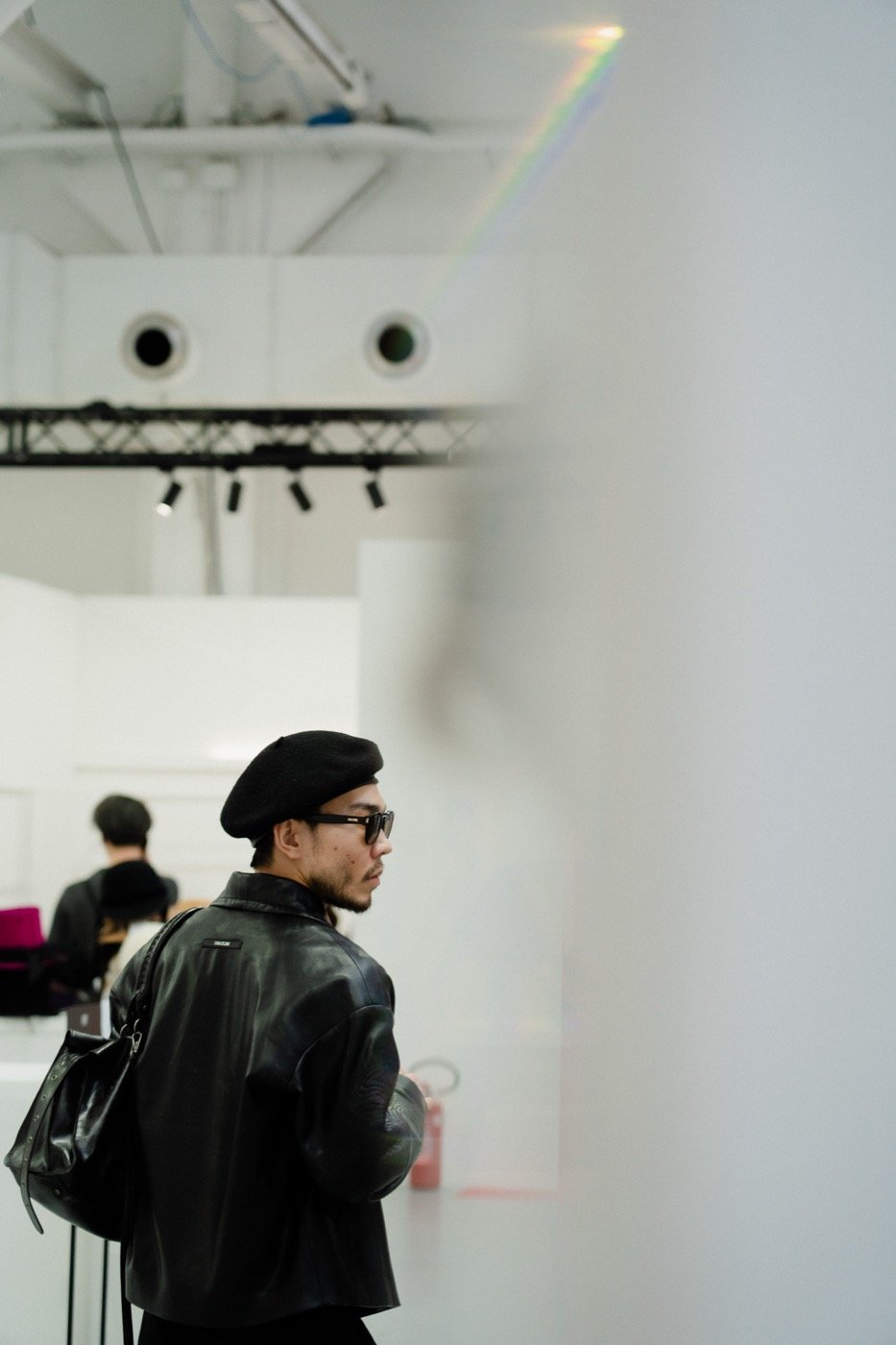 A visitor in a beret and leather jacket walking through the exhibition hall at WHITE Milano
